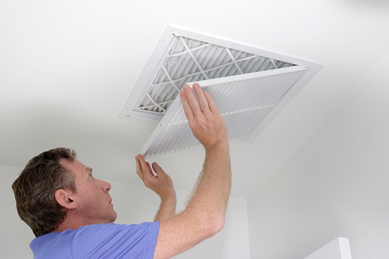 HVAC tech replacing an air filter in ceiling of San Diego home, after air duct cleaning service.